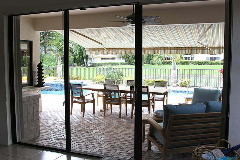 A View Of An Outdoor Space From Inside With A Patio Table And Chairs Next To A Pool