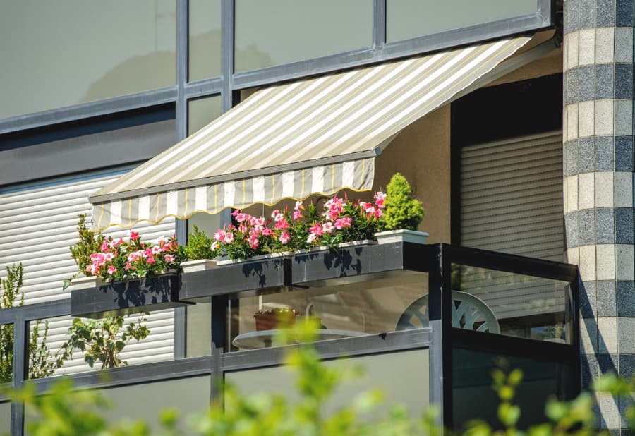 Balcony With Awning Opened And Beautiful Flowers - Covered By Sun-Shield On A Warm Summer Day