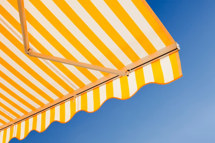 Yellow-And-White-Striped-Awning-Against-A-Blue-Sky Yellow And White Striped Awning Against A Blue Sky